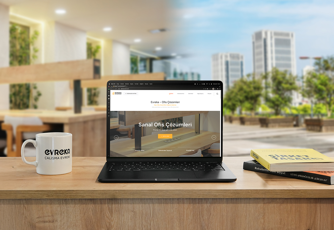 EVREKA sanal ofis — ahşap tezgahta laptop, markalı kupa ve arkada şehir manzarası